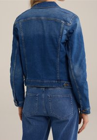 Blå denimjacka med en kortad design, med metallknappar, en klassisk krage och sömnadsdetaljer längs axlarna och ryggen.