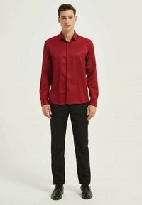 Chemise en satin rouge à manches longues avec col, devant à boutons, et pantalon de costume noir. Les chaussures sont noires avec une finition brillante.
