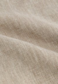 Beige texturerad tyg med fina, parallella ränder och en mjuk yta, som visar en slät, flexibel fall och lättviktig sammansättning.