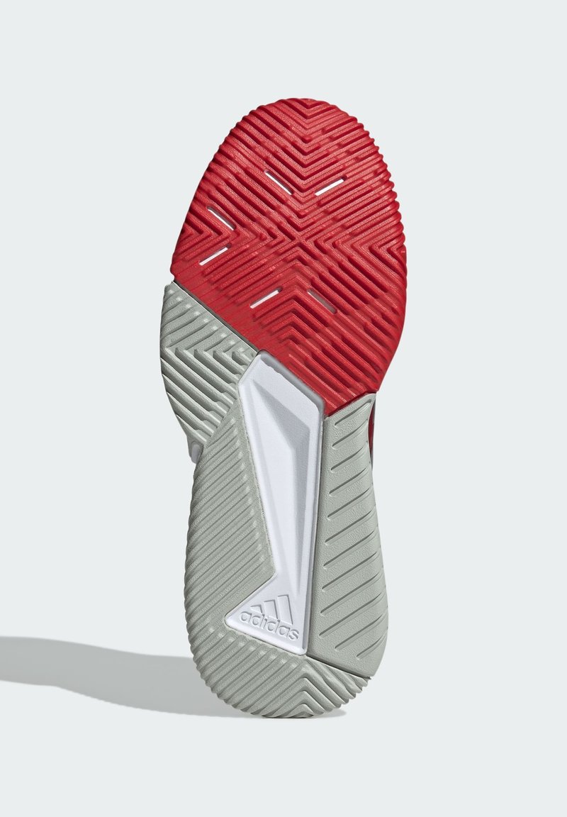 Czerwona i szara podeszwa buta charakteryzuje się teksturowanym wzorem zapewniającym przyczepność, z charakterystycznym białym akcentem i logo Adidas na pięcie.