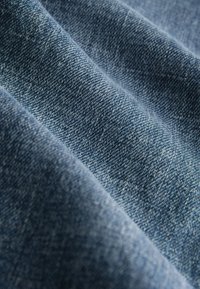 Džínovina v modrých odtieňoch, s textúrovaným tkacím vzorom so zreteľnými stehmi a jemným farebným prechodom. Mäkký, pevný materiál so ľahko ojazdeným povrchom.