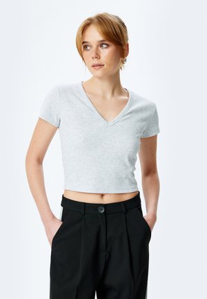 Top corto de ribete en color gris claro, de manga corta y escote en V, combinado con pantalones negros ajustados que tienen un detalle de botón en la cintura.