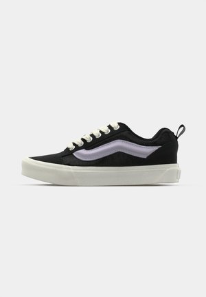 Black canvas sneaker with white laces, a textured upper, lavender side stripe, and white rubber sole. Minimalist design with pull tab.