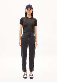 Black t-shirt, high-waisted black jeans, and black shoes with white accents. Model wears a navy cap with a logo. Simple, minimalistic style.