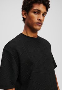 Sweatshirt negru cu textură, decorat cu modele geometrice ridicate, cu guler rotund și mâneci scurte, fabricat dintr-un material moale și confortabil.