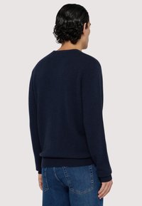 Mörkblå stickad tröja med rund halsringning, ribbade cuffar och nederkant. Slät textur, figurnära silhuett och minimalistisk design.