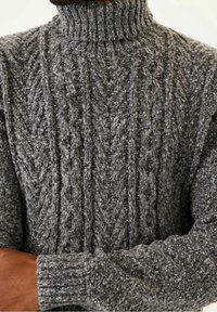 Pull à col roulé gris en maille torsadée présentant des motifs texturés, un col côtelé et un fil épais pour la chaleur. Vue rapprochée des détails du tissu.