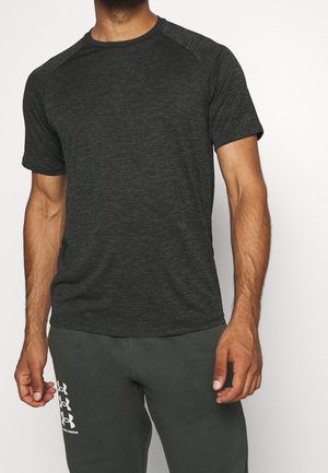 Mann trägt ein dunkelgraues kurzärmeliges Sport-T-Shirt und dunkelgraue Under Armour Trainingshose mit Logo am linken Oberschenkel.