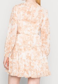 Blommig miniklänning i genomskinligt tyg, med persiko- och vitfärger, långa ärmar, volangsteg och en nyckelhålsknäppning bak med en knapp.