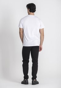 Camiseta de algodón blanca con mangas cortas, corte relajado y escote redondo. Combinada con pantalones negros ajustados y zapatillas negras.