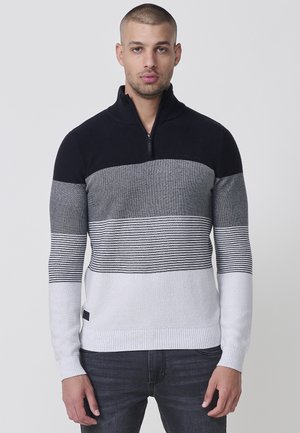 Suéter de punto en azul marino, gris y blanco con un cuello de media cremallera, que presenta rayas horizontales y un dobladillo acanalado. Etiqueta de logo visible en el lateral.