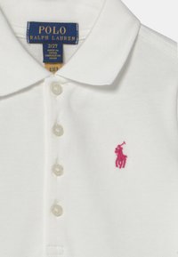 Vit polo t-shirt i texturerad bomull, med en treknappslång placket och en rosa broderad polo-spelare-logga på vänster bröst.