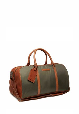 Sac de sport en toile verte avec des accents en cuir marron, comportant des poignées doubles, une bandoulière amovible et une étiquette.