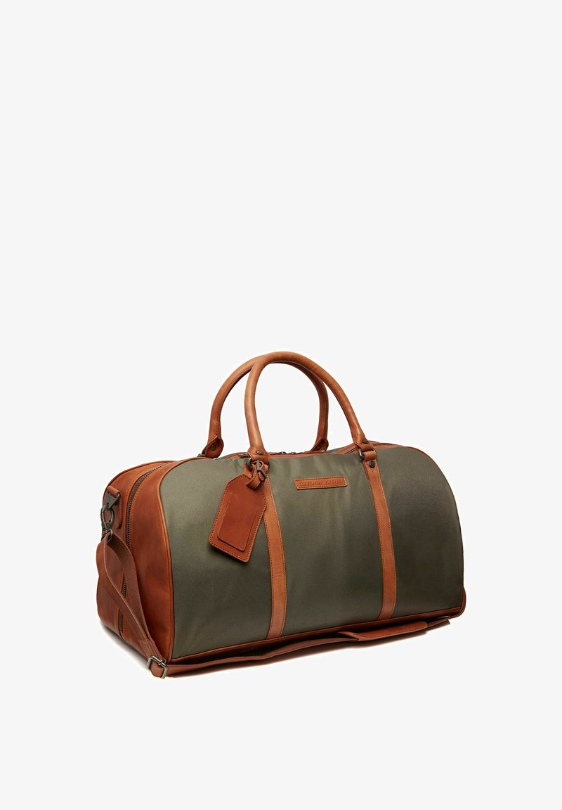 Sac de sport en toile verte avec des accents en cuir marron, comportant des poignées doubles, une bandoulière amovible et une étiquette.