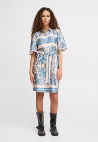 Rochie camasa de culoare piersici deschis, cu modele florale albastre si paisley, maneci scurte, talie evidentiata cu brau, si asortata cu botine negre cu toc.