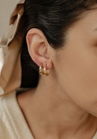 Boucles d'oreilles en or avec un design à trois niveaux. Texture lisse, finition brillante et une courbe subtile à chaque niveau, mettant en valeur le lobe de l'oreille.
