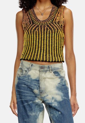 Personne portant un crop top tricoté multicolore sans manches avec des rayures verticales et un jean tie and dye bleu et blanc taille haute.