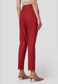 Czerwone spersonalizowane spodnie o wysokim stanie i zwężających się nogawkach. Posiadają dwie tylne kieszenie zapinane na guziki oraz gładką fakturę.