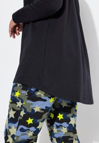 Zwart langlijnig shirt gecombineerd met blauw en groen camouflagebroeken met gele sterren en een getailleerde pasvorm. Zachte stof met een ontspannen silhouet.