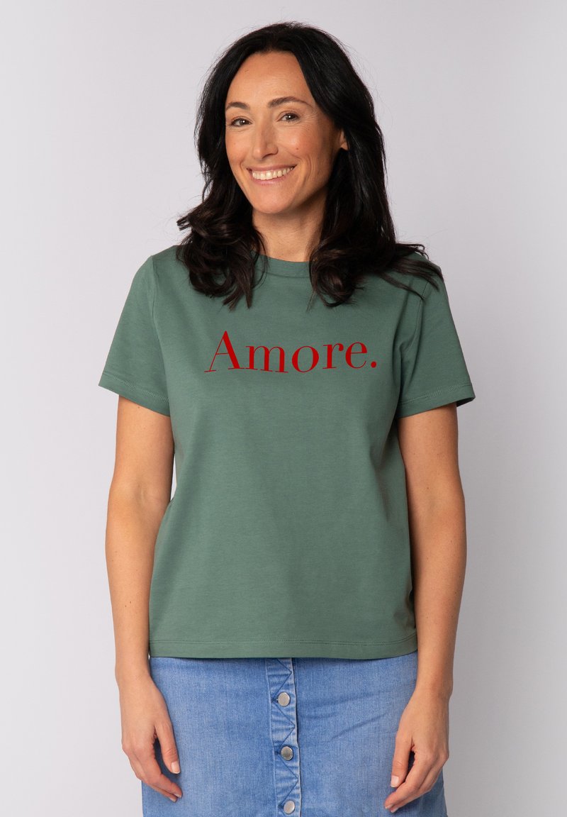 T-shirt en coton vert avec le texte imprimé rouge "Amore" sur le devant, col rond et manches courtes. Associé à une jupe en denim.