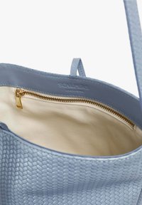 Geantă de voiaj din piele bleu deschis, cu un exterior texturat, fermoar auriu și căptușeală din țesătură bej. Dispune de un buzunar interior cu închidere cu fermoar.