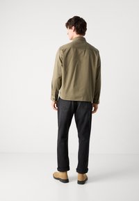 Olive green long-sleeve shirt with a button-down collar, paired with dark gray jeans and tan ankle boots. Simple design, no visible patterns.