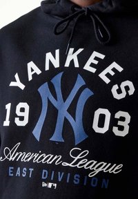 Felpa nera con cappuccio caratterizzata da un grande testo "YANKEES" in bianco e blu, un logo grafico, l'anno "1903" e "American League East Division" in corsivo bianco.
