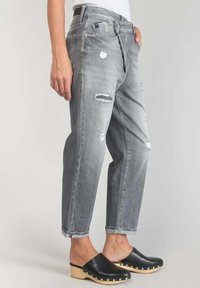 Harmaat kulutetut farkut, joissa on löysä istuvuus, repeämillä koristellut yksityiskohdat ja käännetyt lahkeet. Yhdistetty mustiin klomposseihin, korostaen rentoa tyyliä.