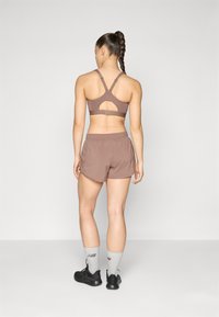 Soutien-gorge de sport marron avec un design découpé, associé à un short marron assorti. Porté avec des chaussettes grises et des chaussures de sport noires.
