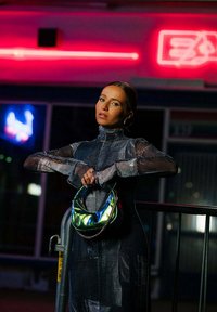 Borsa metallica con texture iridescente e tracolla a catena, indossata con un vestito in denim aderente a collo alto caratterizzato da una finitura stampata.