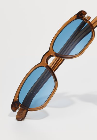 Ochelari de soare din plastic maro cu un cadru geometric unic, având lentile albastre și brațe texturate.