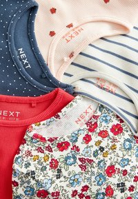 Vier Oberteile in verschiedenen Farben: marineblau mit weißen Punkte, hellrosa mit roten Punkten, rotes Rippenmuster und Blumendruck. Die Etiketten sind auf jedem sichtbar.