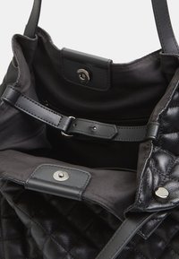 Interno di una borsa a spalla nera in pelle trapuntata con una fodera in tessuto morbido; presenta una chiusura a scatto e una tracolla regolabile.