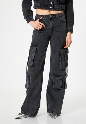 Pantalons cargo en denim noir avec des jambes larges, comportant plusieurs grandes poches et une finition légèrement délavée. Des poches zippées sont incluses.