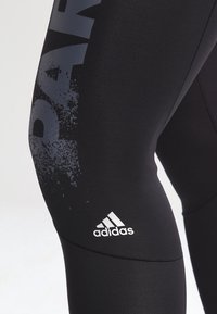 Mustat urheiluleggingsit, joissa on teksturoitu kuvio, harmaat roisketahrat ja sana "PAR" painettuna pystyyn. Sisältää valkoisen Adidas-logon.