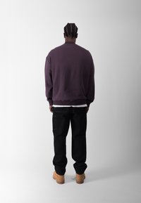 Lilla crewneck sweatshirt, sorte bukser med sidelommer og brune arbejdssko. Simpelt, afslappet fit; ensartet tekstur uden fremtrædende mønstre.