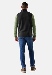 Gray fleece vest with a high collar over a green long-sleeve shirt, paired with blue jeans and brown shoes, viewed from the back.