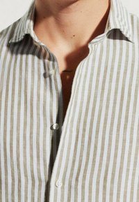 Gestreiftes Hemd mit beigen und weißen Streifen, ausgestattet mit einem Button-Down-Kragen und kleinen runden Knöpfen. Der Stoff wirkt leicht und strukturiert.