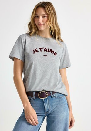 Grå bomulds t-shirt med korte ærmer og "JE T'AIME PARIS" trykt i bordeaux bue. Sammen med blå jeans og et brunt bælte med en guldbuckle.