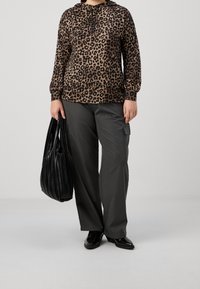 Felpa con stampa leopardata in marrone e nero, abbinata a pantaloni cargo grigi larghi. Borsa a tracolla nera plissettata. Scarpe nere a punta.