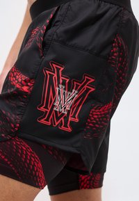 Μαύρο και κόκκινο αθλητικό σορτς με στρωματοποιημένο σχέδιο και τολμηρά κόκκινα διακοσμητικά μοτίβα, με μεγάλο στυλιζαρισμένο λογότυπο "M" στην πλαϊνή τσέπη.