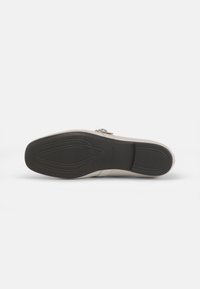 Suola della scarpa in gomma nera con battistrada a motivo.Parte superiore in materiale beige chiaro, con dettaglio di fibbia laterale e finitura morbida.