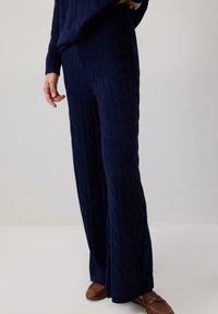 Jūras zilas adītas atpūtas bikses plaša kāju dizainā, ar teksturētu rakstu un brīvu piegriezumu. Saskaņojot ar brūnām slīdējošām kurpēm.