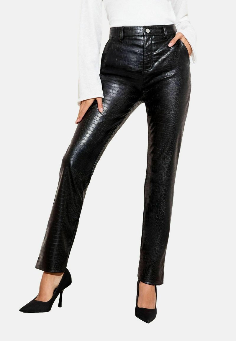 Crne hlače od umjetne kože s teksturom krokodilske kože, visokim strukom, prednjim džepovima i uskim krojem, uparene s crnim štiklama.