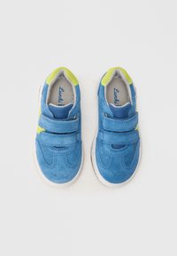 Siniset mokkanahkaiset lenkkitossut, joissa keltaiset yksityiskohdat ja tarrakiinnitys. Pyöristetty varvasmuoto ja pehmeä, tekstiilipintainen sisäpinta. Valkoiset kumi-pohjat.