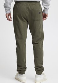 Olivgrüne Jogginghosen mit elastischem Bund, Gesäßtasche und einer weichen Textur. Kombiniert mit weißen Sneakern, zeigen sie eine lockere Passform durch die Beine.