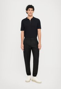 Marineblå kortærmet polo med lynlåskrave, parret med sorte cargo-bukser med sidelommer og hvide sneakers med tyk sål.