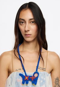 Collar de ganchillo azul con acentos florales y un colgante redondo. Presenta intrincados trabajos en cuentas y detalles texturizados.