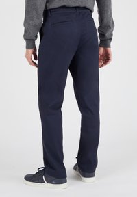 Marineblauwe broek van gladde stof, met een slim fit, rechte pijpen en twee achterzakken. Gdragen met donkere sneakers.