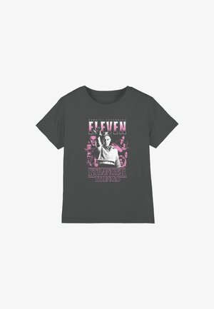 Dunkelgraues T-Shirt mit der Stranger Things-Figur Eleven, die die Hand erhebt, umgeben von kleineren Charakterbildern in rosa Tönung und fettem Text.